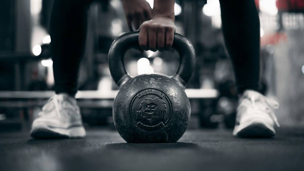 Mão a segurar um kettlebell no chão do ginásio