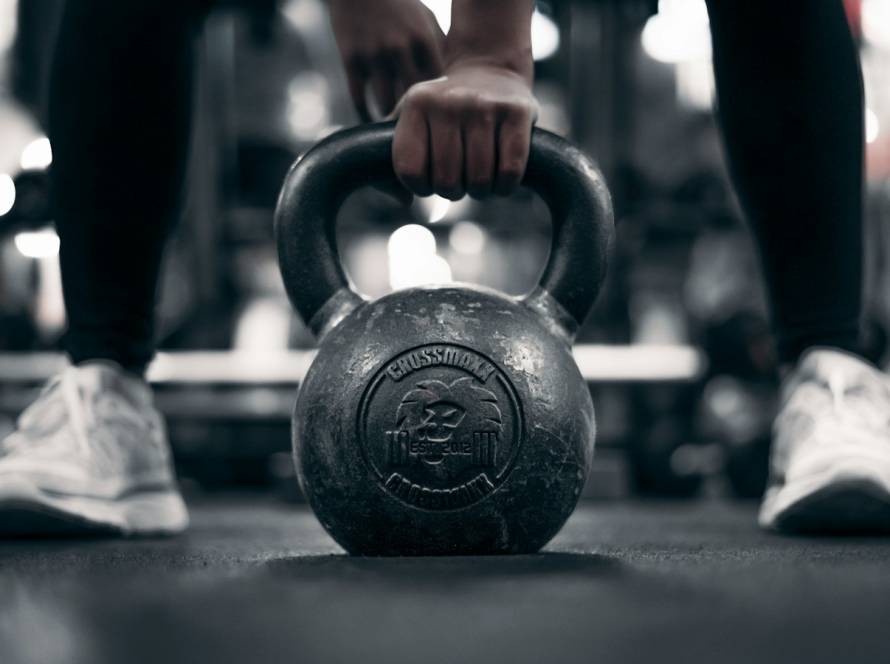Mão a segurar um kettlebell no chão do ginásio